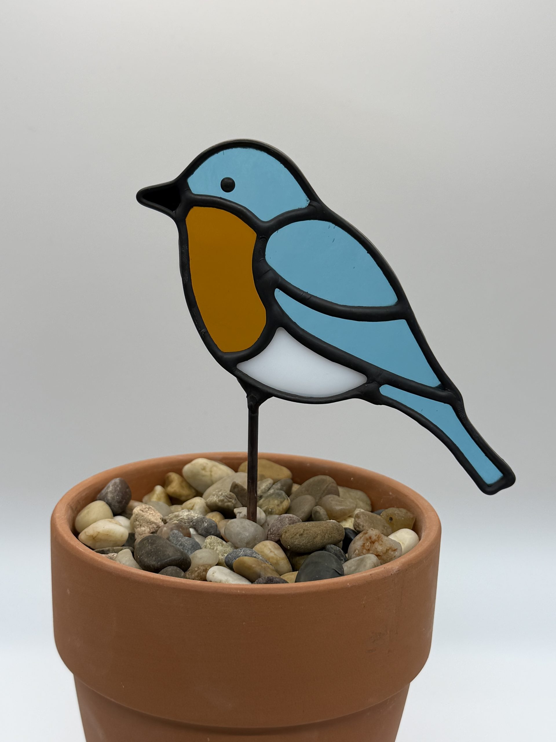 blue bird stained glass plant stake. blue body, dark amber belly, white underbelly.